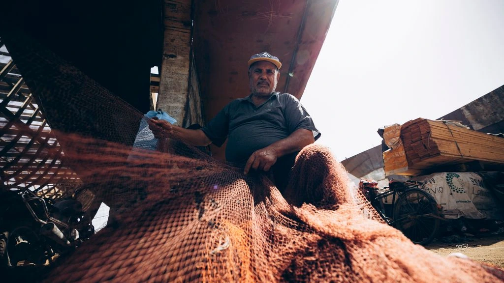 Fishing port in Cádiz with fishermen mending trawl nets on the dock.